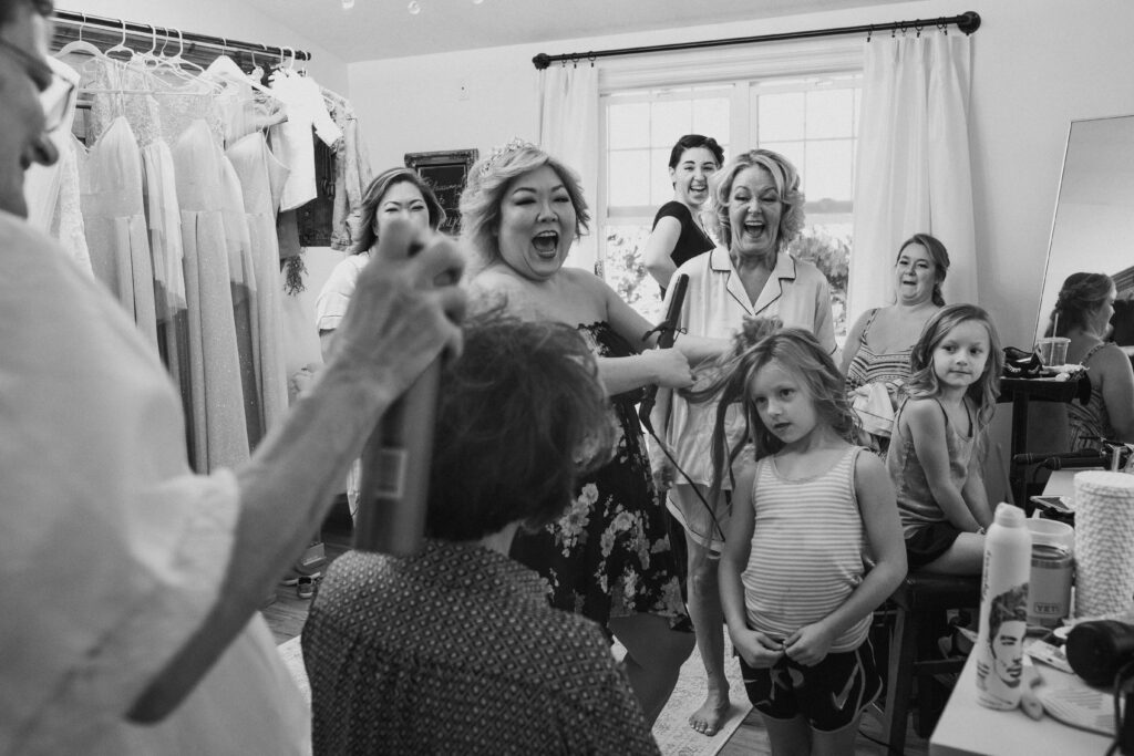 A bride laughing while getting ready in a room full of other girls laughing